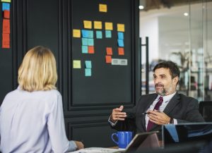 A man talks to a woman in front of a Scrum board