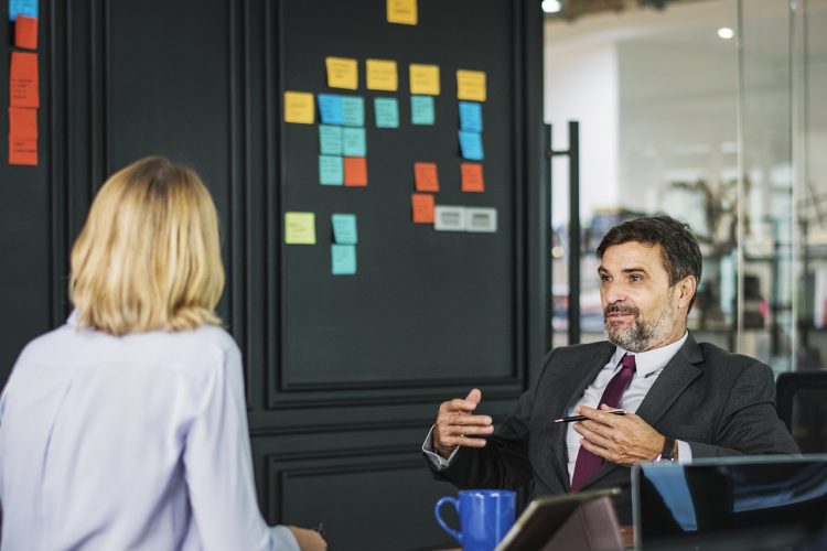 A man talks to a woman in front of a Scrum board